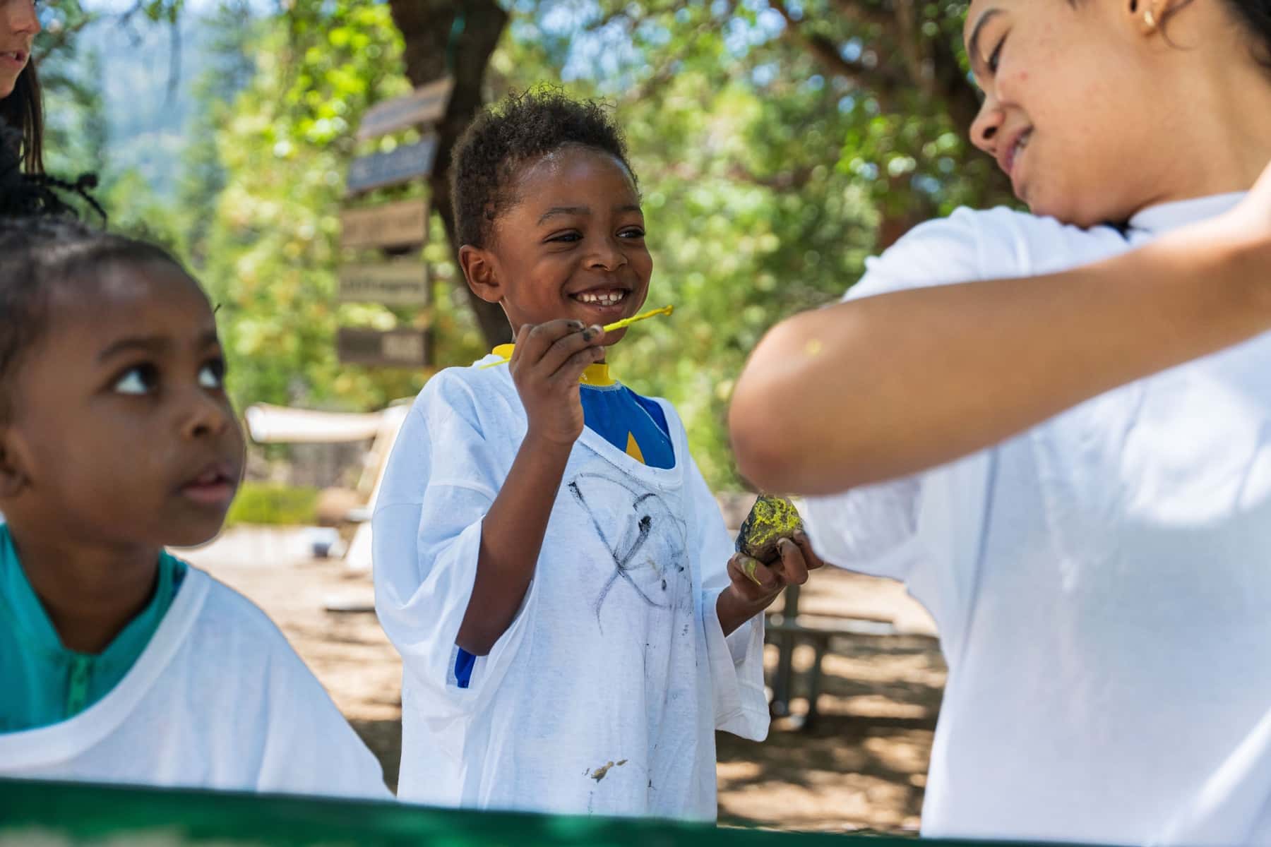 A boy laughs as a teenager hands him a painted rock at the camp craft table