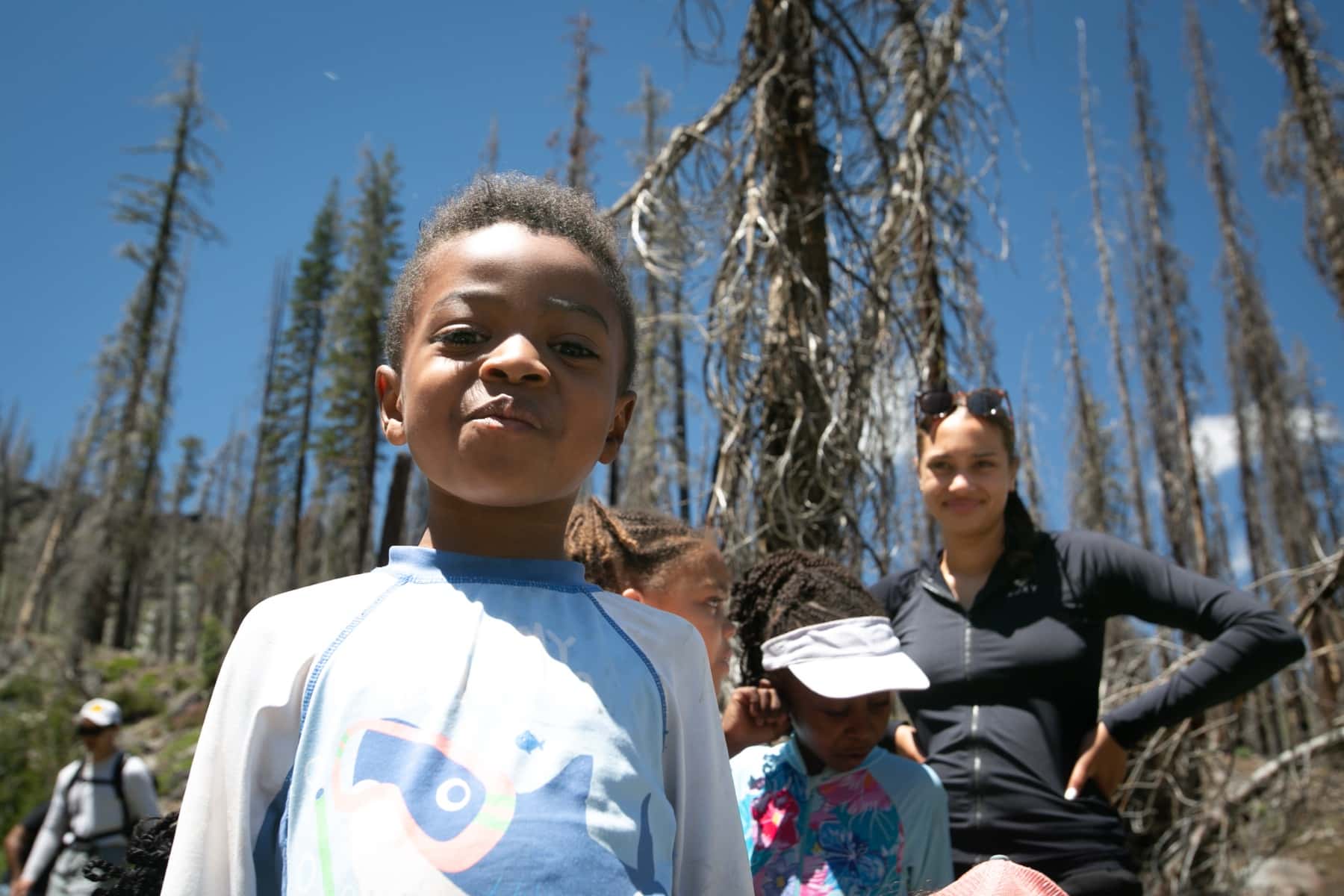 Children and adults hiking a trail together beneath standing snags at Lassen Volcanic National Park