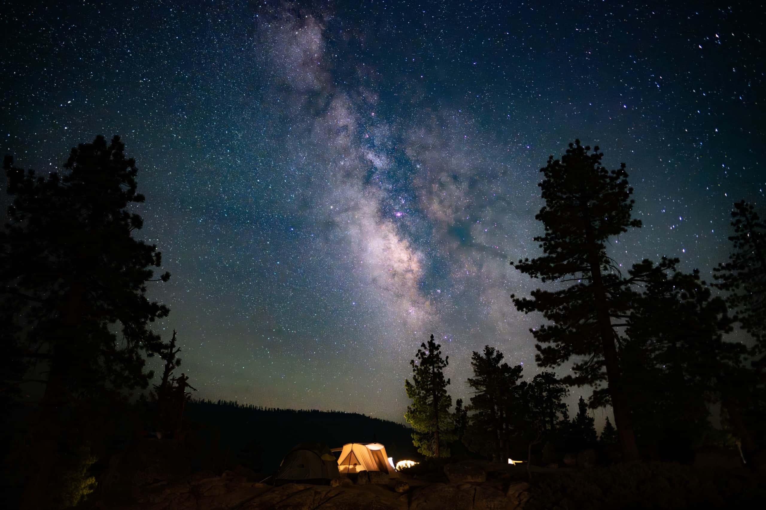 The Milky Way arching over a glowing canvas wall tent at the Spicer Reservoir camp