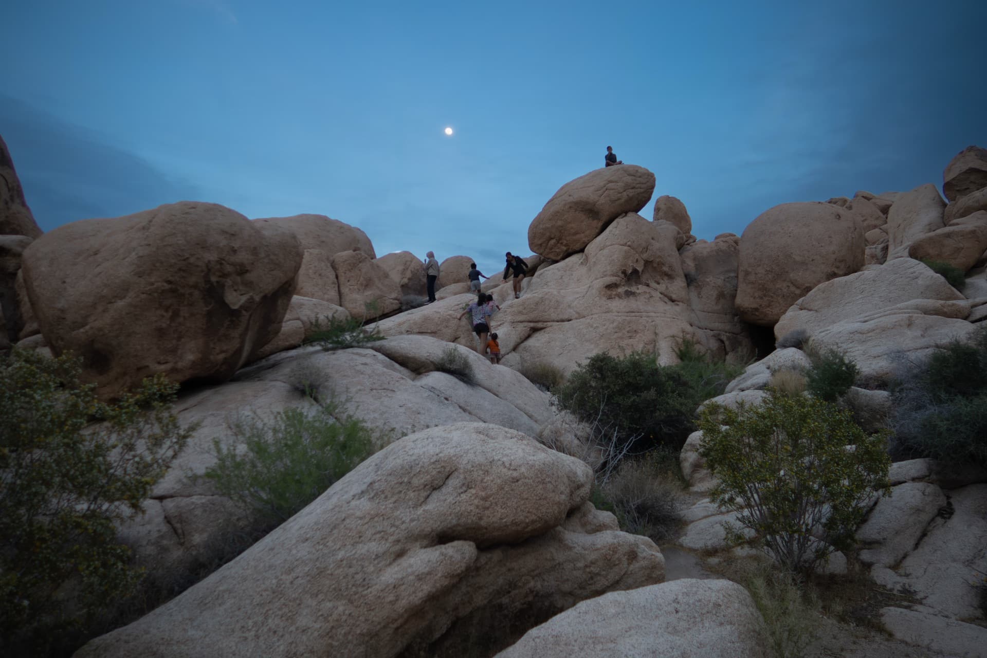 Group climbing the boulders at dusk under a full moon