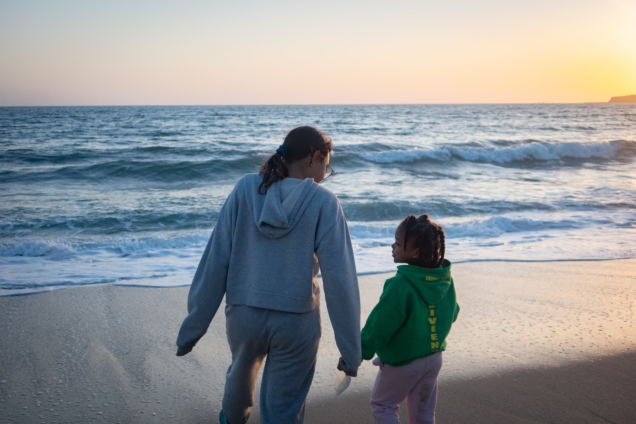 Adult and child walking hand-in-hand on a beach at sunset