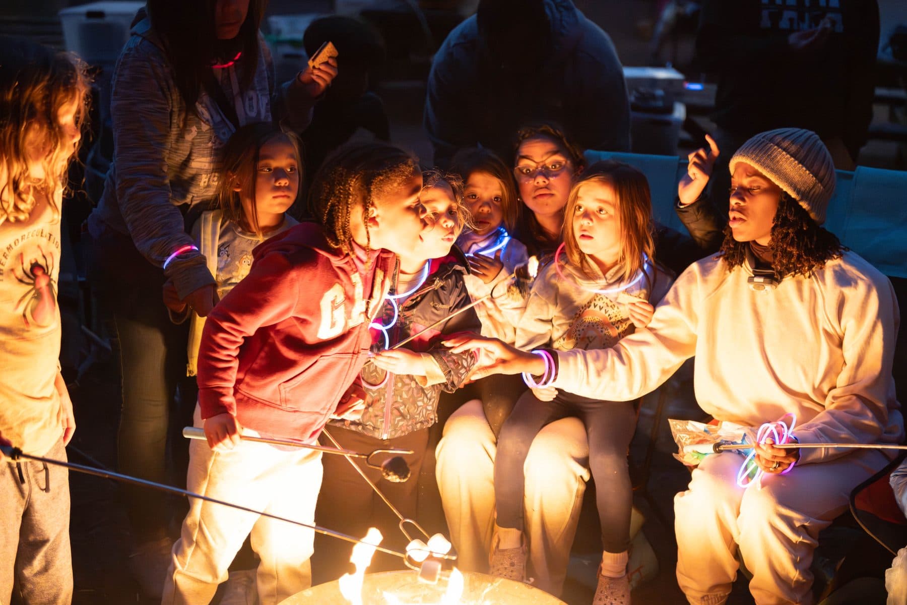 Children lit by firelight passing glow sticks around the campfire at Humboldt Redwoods