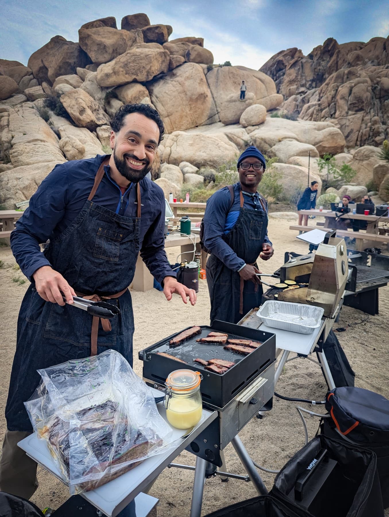 Two Outdoorithm hosts in aprons working the grill at the camp kitchen in Joshua Tree