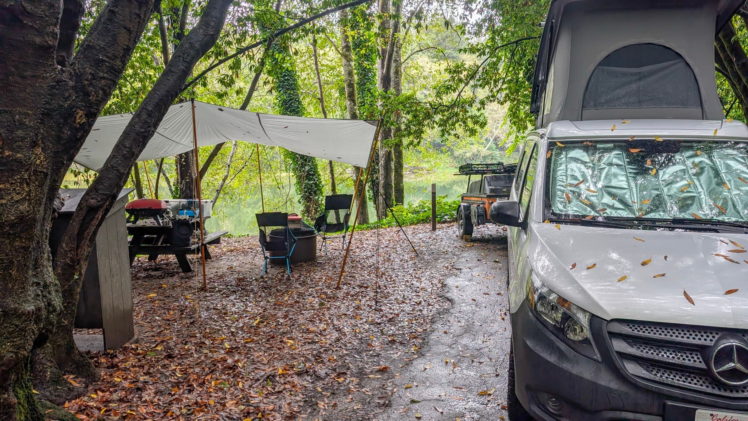 A tarp rigged over the camp kitchen at a rain-soaked campsite, leaves scattered across the wet ground