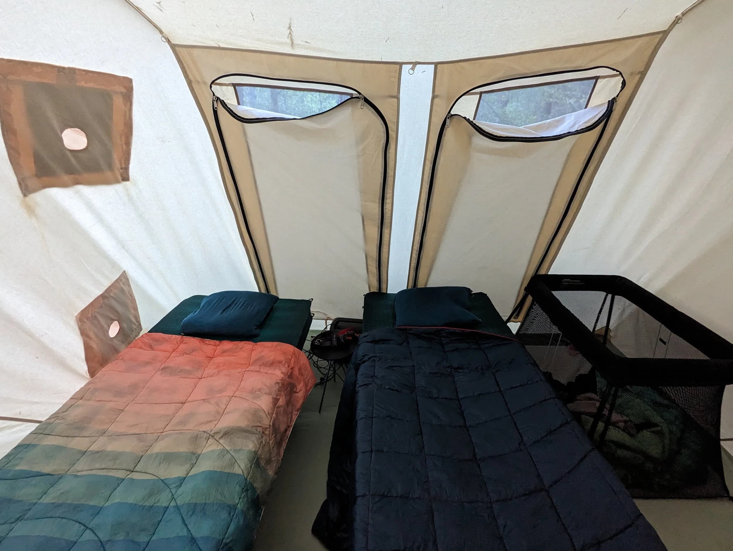 The inside of a canvas tent set up with cots, sleeping bags, and pillows